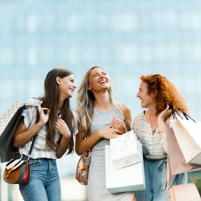 a group of women laughing while holding shopping bags