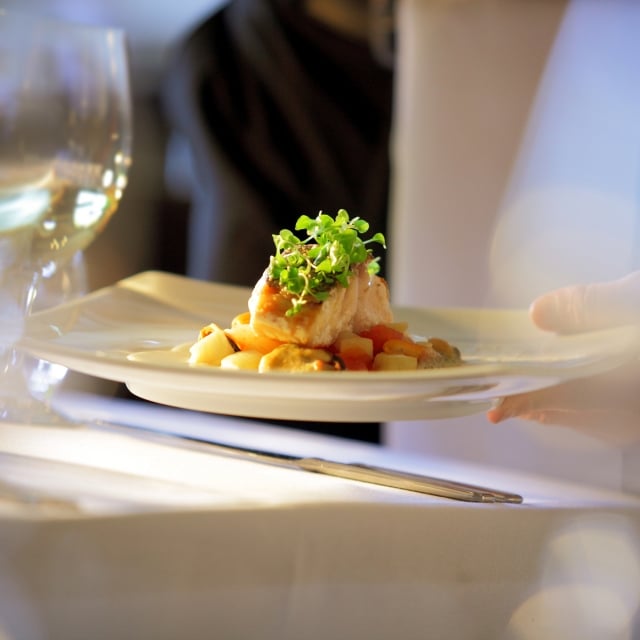 A close up of a dish being placed on a table by the waiter